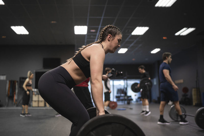 Woman picking barbell with people exercising in background at gym