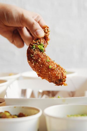 Close-up of hand holding chicken wing in plate