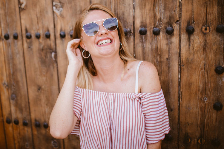 Blonde woman with sunglasses laughing and touching her hair