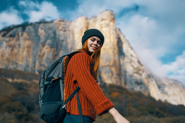 Smiling young woman standing against mountain against sky