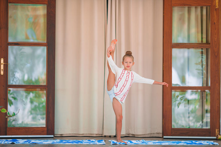 Full length of girl stretching against window