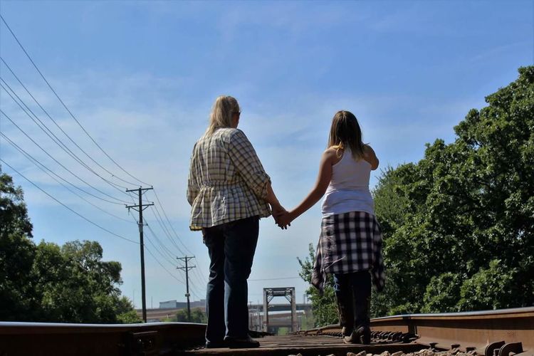 Rear view of friends with holding hands standing on railroad track against sky