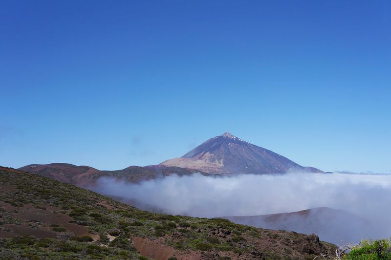 Scenic view of volcanic mountain against blue sky