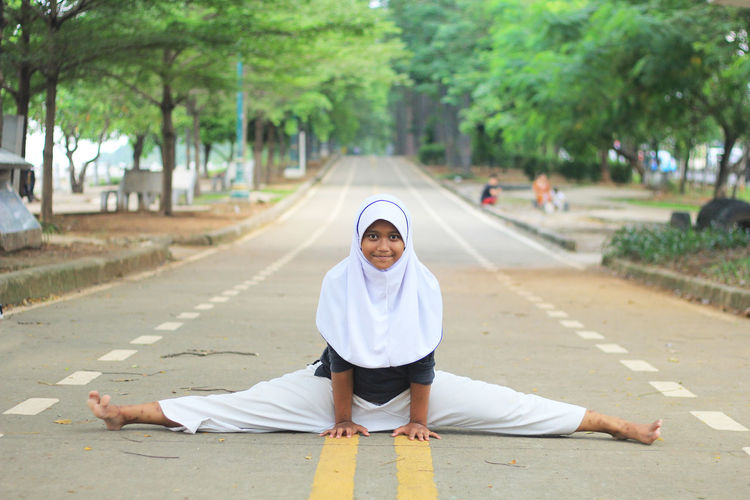 Portrait of girl in hijab doing splits on road