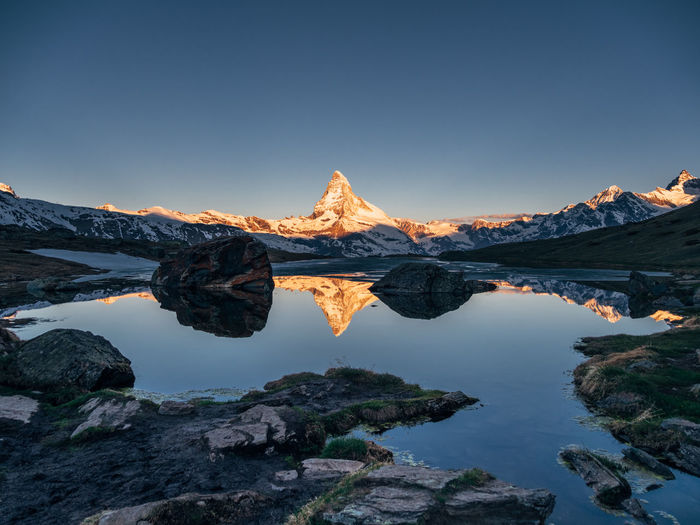 Reflection of matterhorn mountain in lake against clear sky during sunset