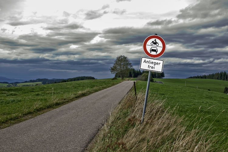 Information sign on road amidst field against sky