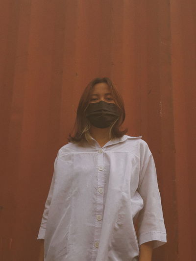 Portrait of woman wearing mask standing against wall