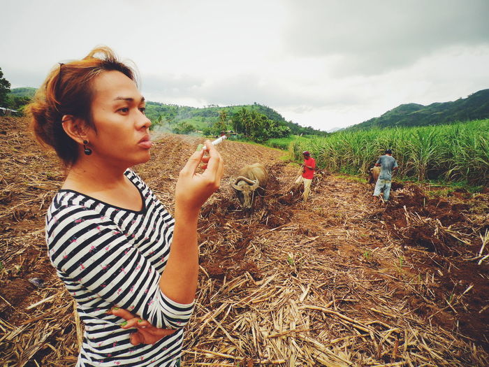 Woman smoking on agricultural field against sky