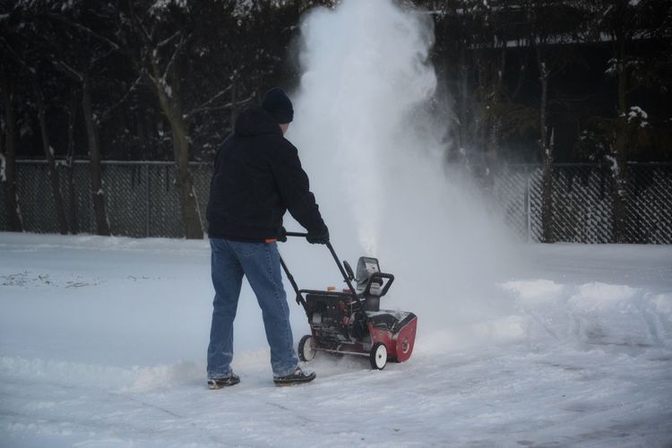 Rear view of man using a snowblower on snow covered land