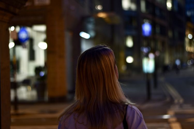 Rear view of woman standing against illuminated city at night