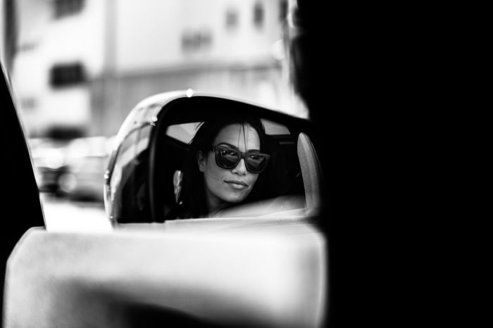 Reflection of woman wearing sunglasses in side-view mirror of car
