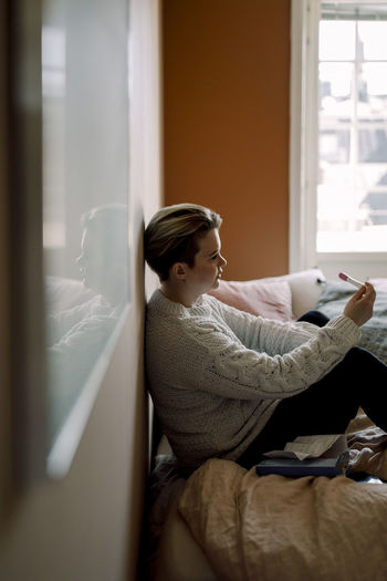 Side view of young woman sitting on bed at home