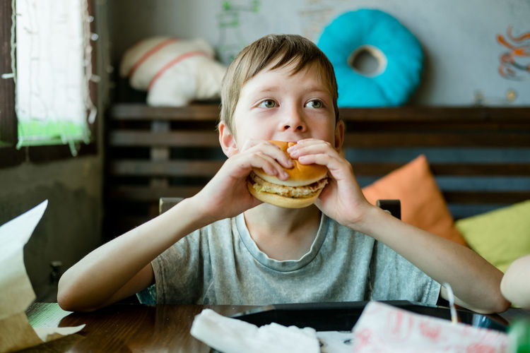 Boy eating a big burger with a cutlet. hamburger in the hands of a child. delicious chicken burger.