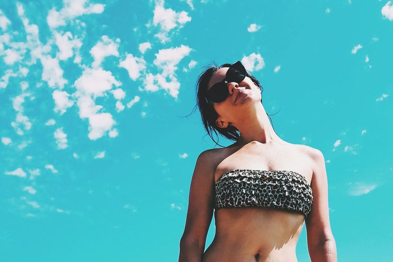 Low angle view of woman wearing sunglasses and bikini top against sky during sunny day
