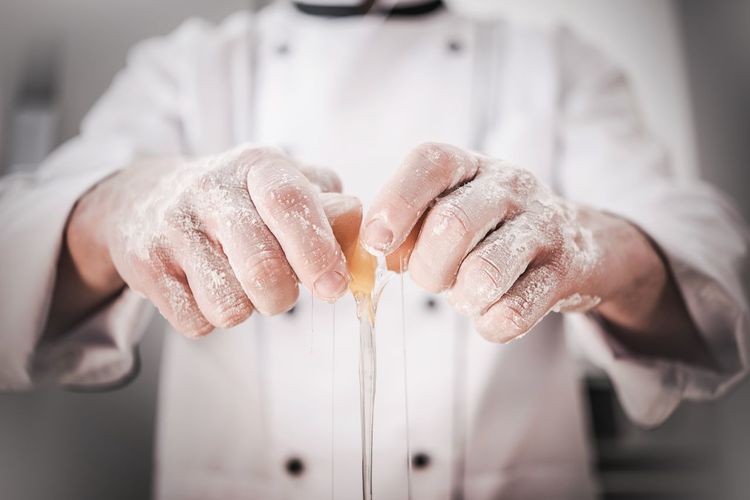 Midsection of male chef breaking egg in kitchen