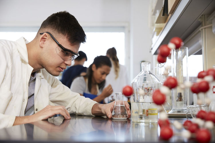 Confident young male chemistry student by friends in laboratory at university