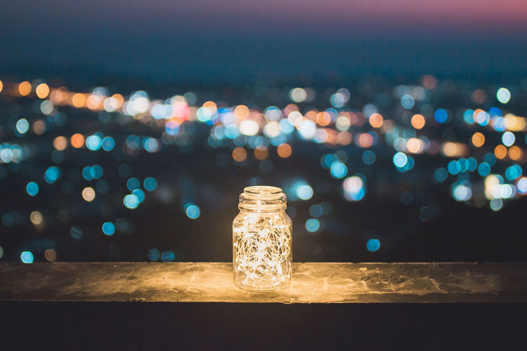 Close-up of illuminated string lights in glass jar on retaining wall at night