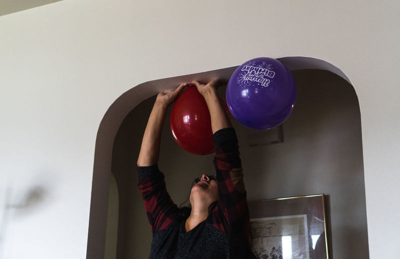 Rear view of woman holding balloons against wall at home