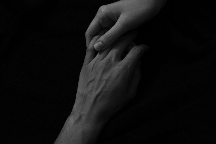 Cropped image of people holding hands against black background
