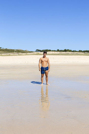 Full length of shirtless man walking on beach