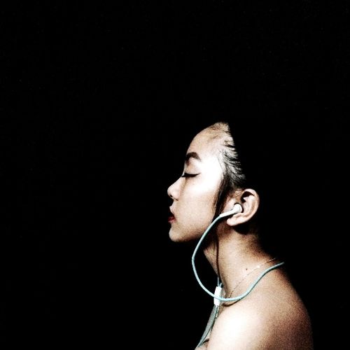 Side view of topless woman listening music against black background