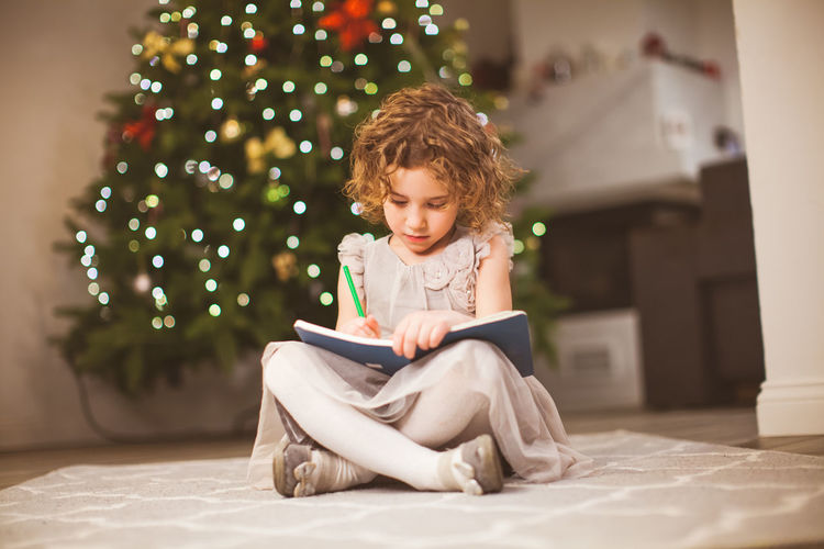 Boy looking away while sitting on christmas tree at home