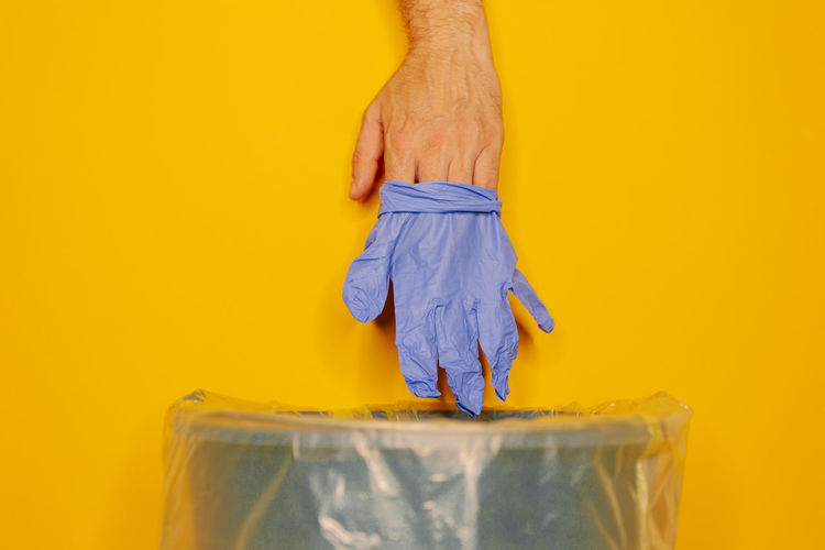 Close-up of hand holding plastic against yellow background