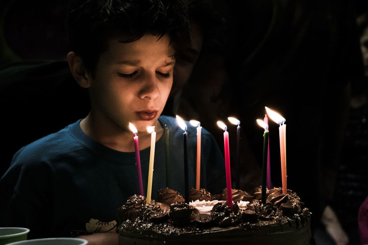Close-up of boy blowing candles on birthday cake in dark room