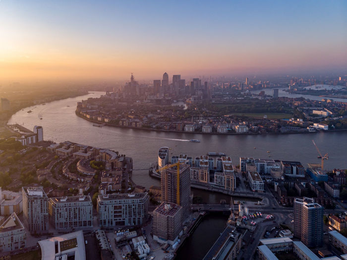 Aerial view of buildings by river against sky in city during sunset