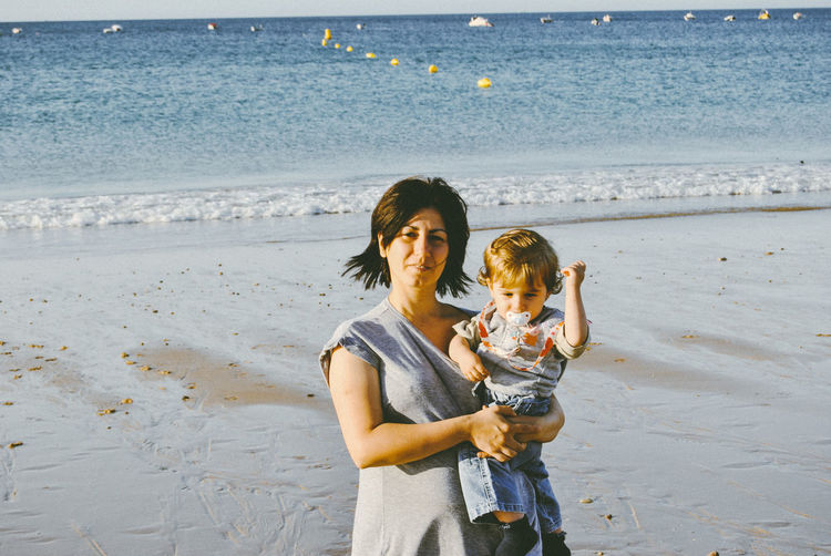 Portrait of mother carrying son while standing at beach