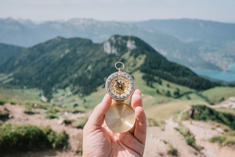 Cropped hand holding compass against mountains