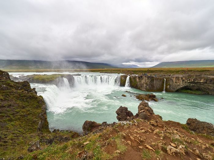 Scenic view of waterfall against cloudy sky