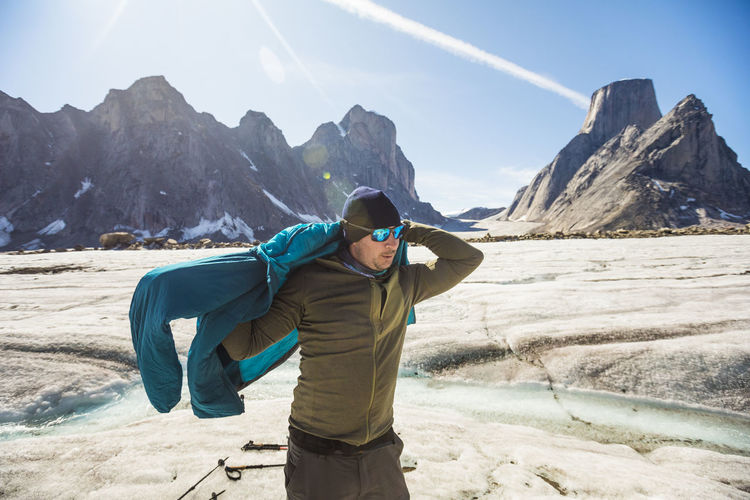 Mountaineer puts on warm jacket in glacial mountain landscape.