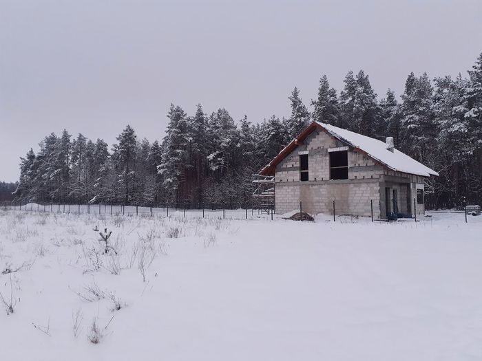 House on snow covered field by trees against sky