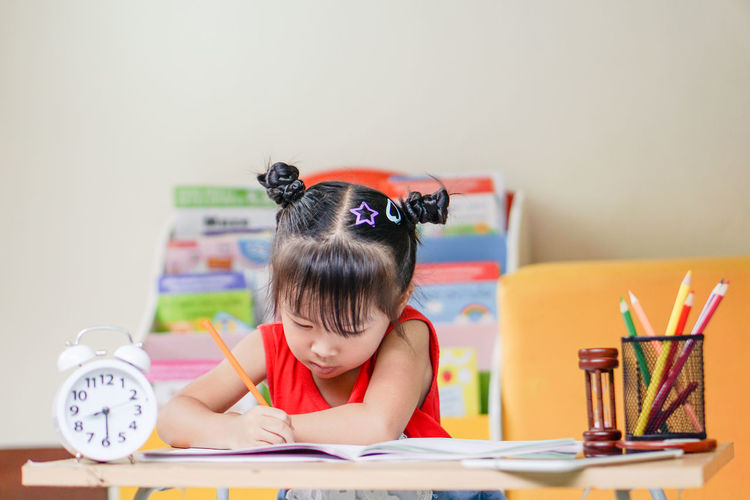 Cute girl drawing on paper while sitting on table at home