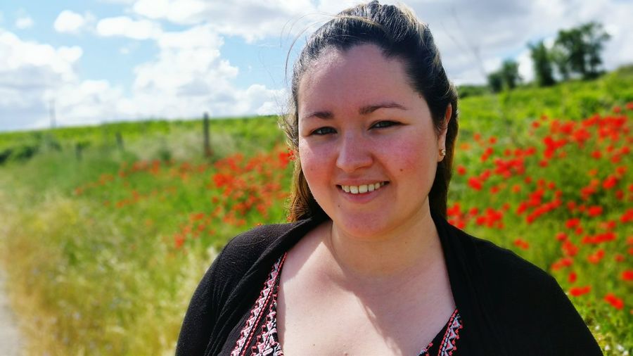 Portrait of smiling woman standing against poppy field