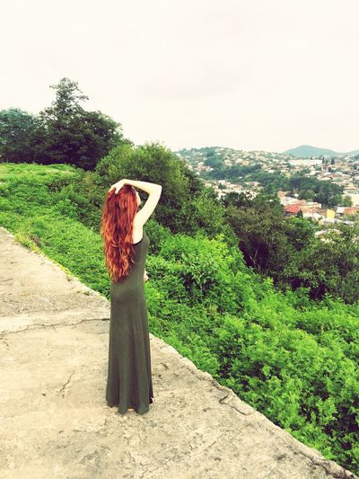 Full length of redhead woman with hand in hair while standing on cliff