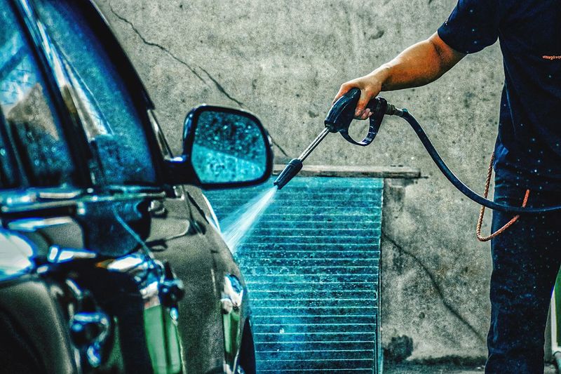 Midsection of man washing car with hose