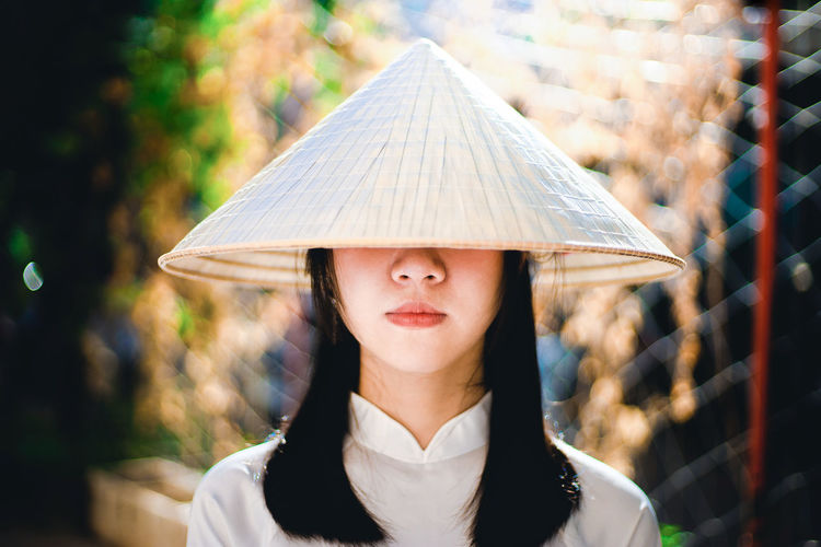 Portrait of young woman wearing conical hat standing against blurred background
