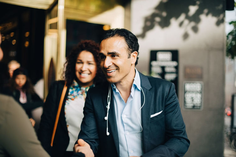 Smiling mature businessman greeting businesswoman while standing by female colleague against building