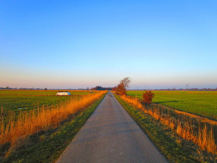 Road passing through agricultural field against clear sky