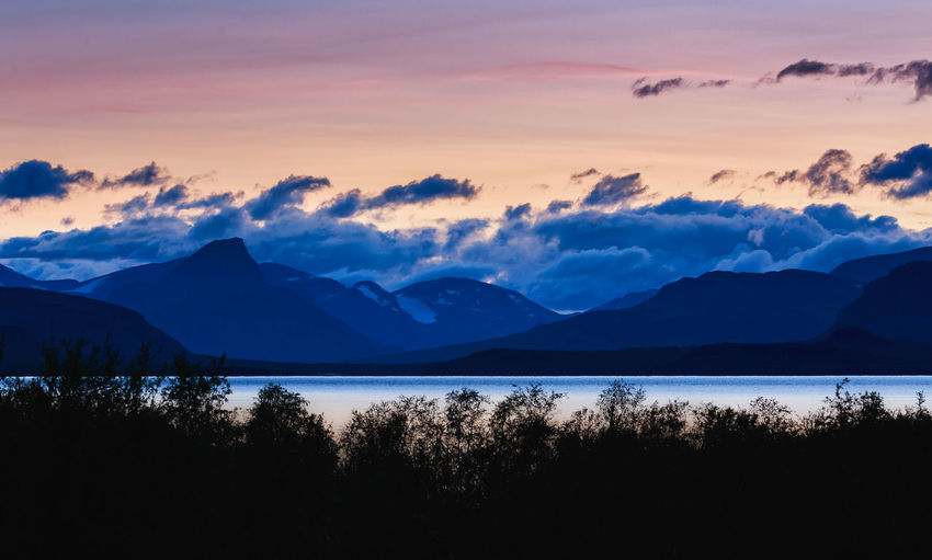 Scenic view of lake by silhouette mountains against sky during sunset