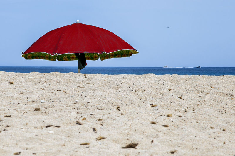 Red umbrella on beach against clear sky