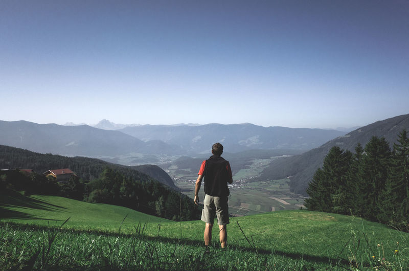 Rear view of man looking at mountains against clear blue sky