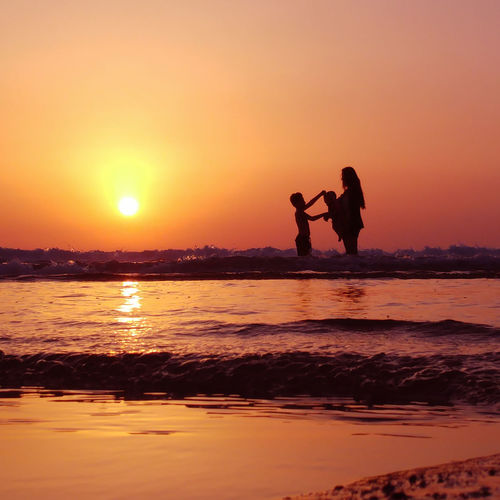 Silhouette couple standing at beach during sunset