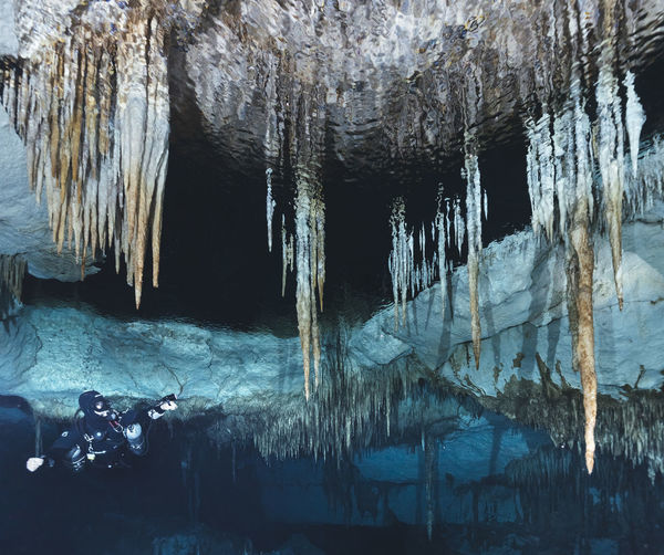 Low angle view of man scuba diving below stalactites in sea