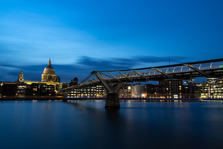 Illuminated bridge over river against blue sky at night