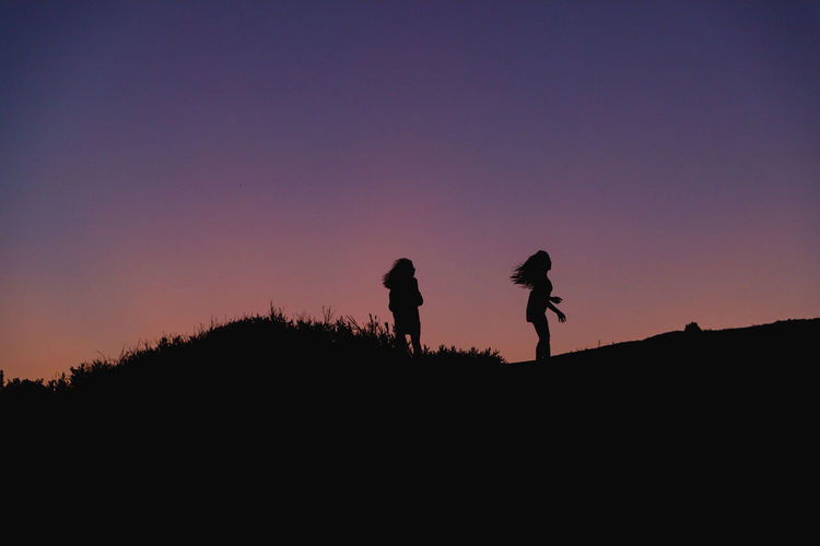 Silhouette of two women walking in a field against a sky during sunset