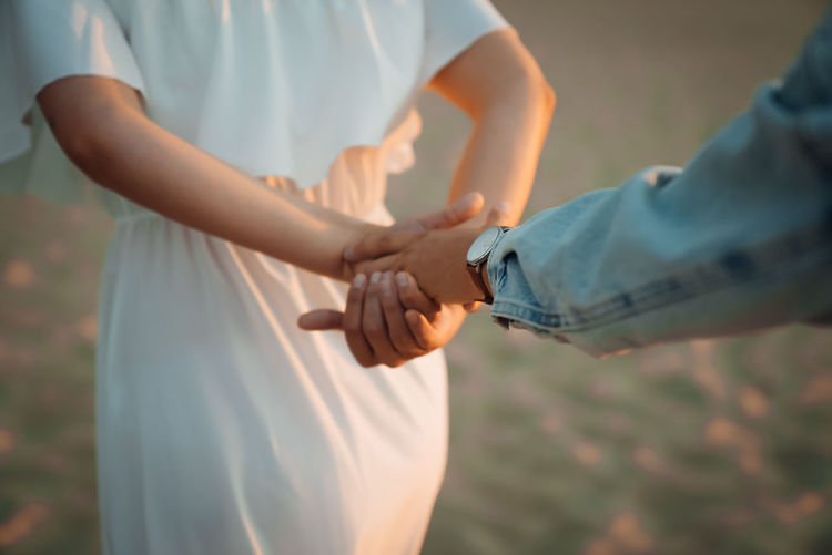 MIDSECTION OF MAN AND WOMAN HOLDING HANDS WHILE STANDING OUTDOORS