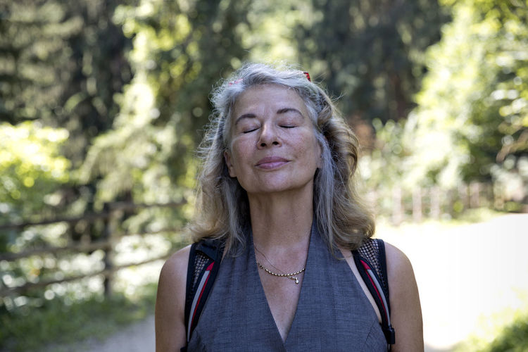 Senior woman with eyes closed inhaling fresh air in forest